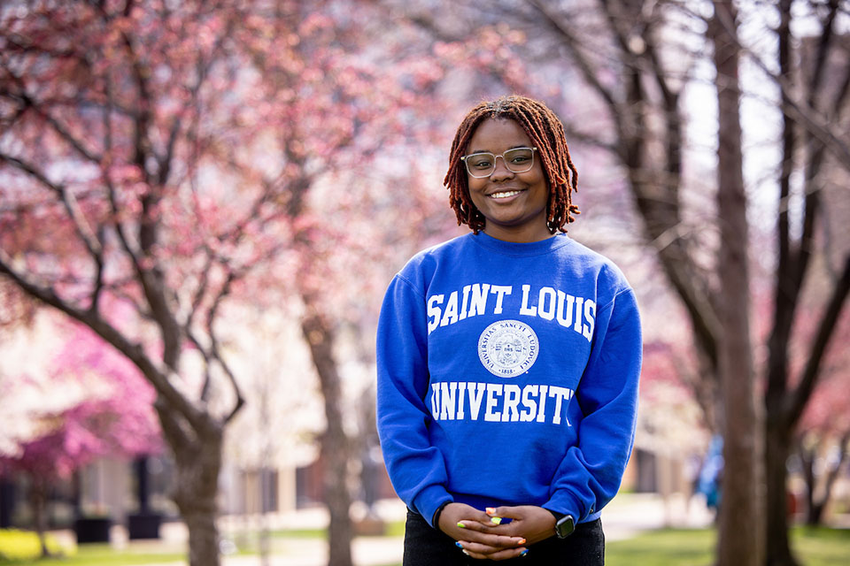  A student poses for a photo outside on campus wearing a blue sweatshirt that says "Saint Louis University."