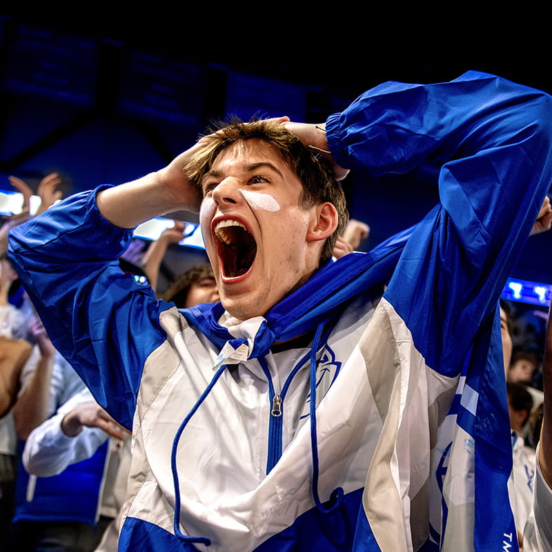 A student cheers while holding his hands on his head.