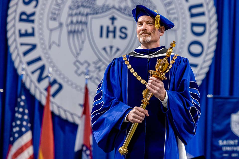 a man in a blue graduation gown holding a gold object